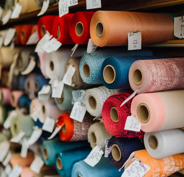 Fabric rolls displayed in a sourcing department with labeled tags and color swatches.png
